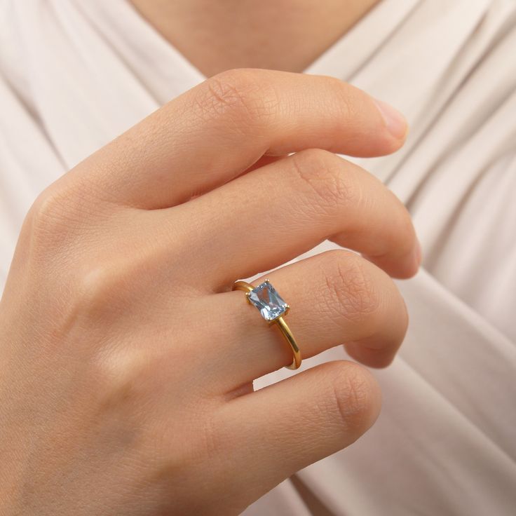 a woman's hand wearing a gold ring with an aqua blue topazte