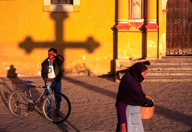 two people standing next to each other near a building with a cross on the wall