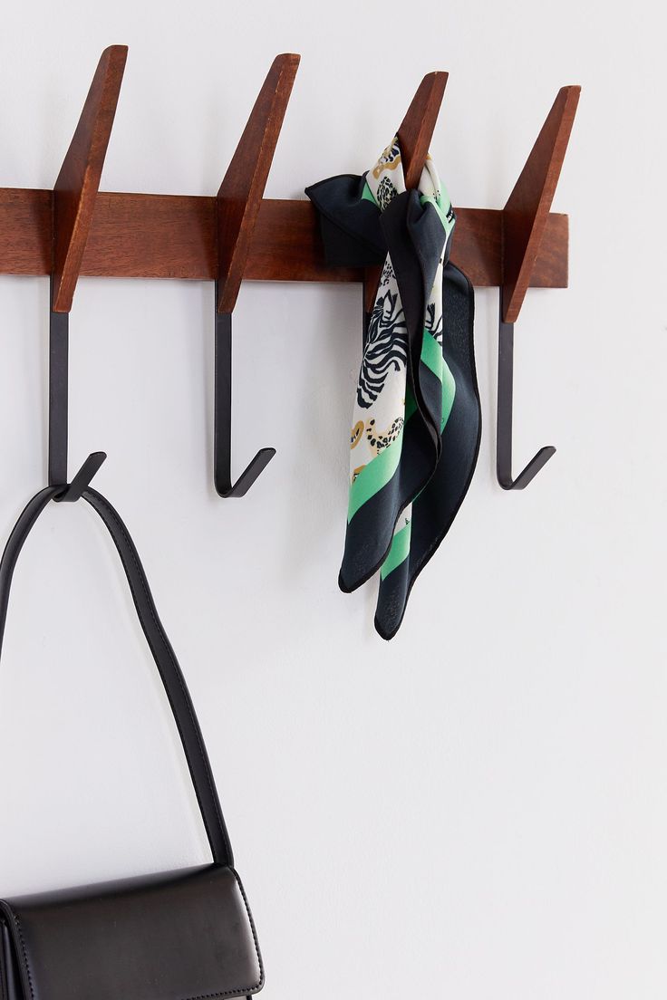 two scarfs hanging from hooks on a wall next to a handbag and purse