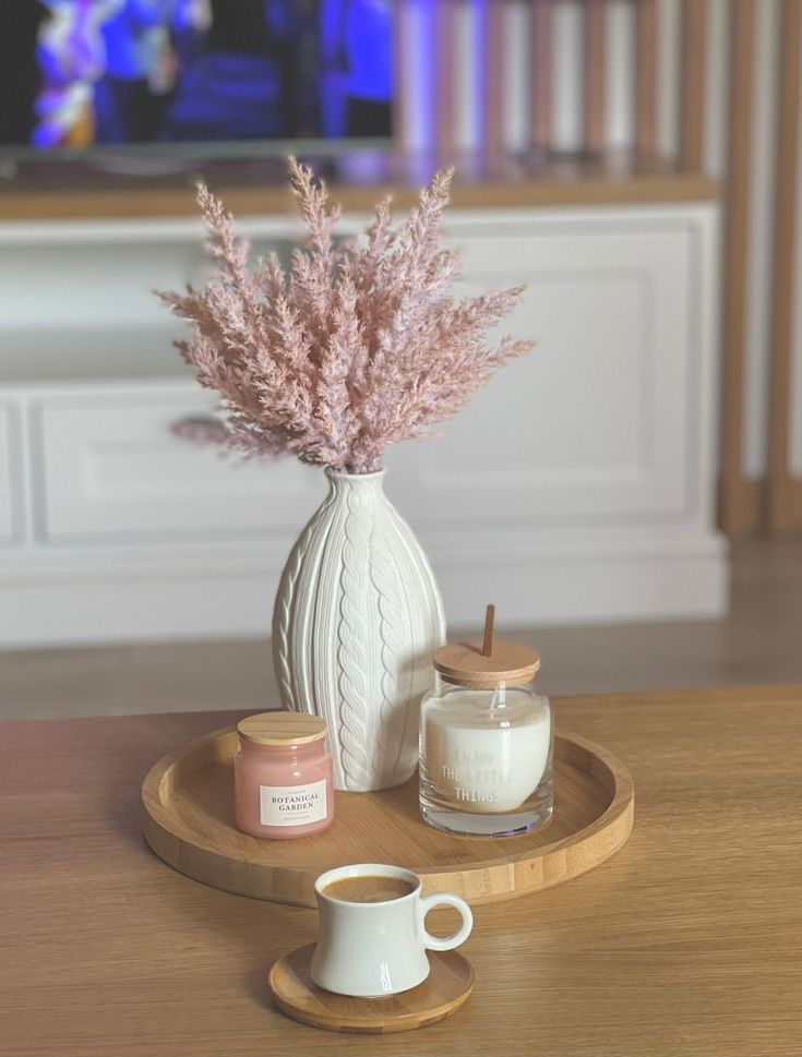 there is a vase with pink flowers in it and two cups on the table next to it