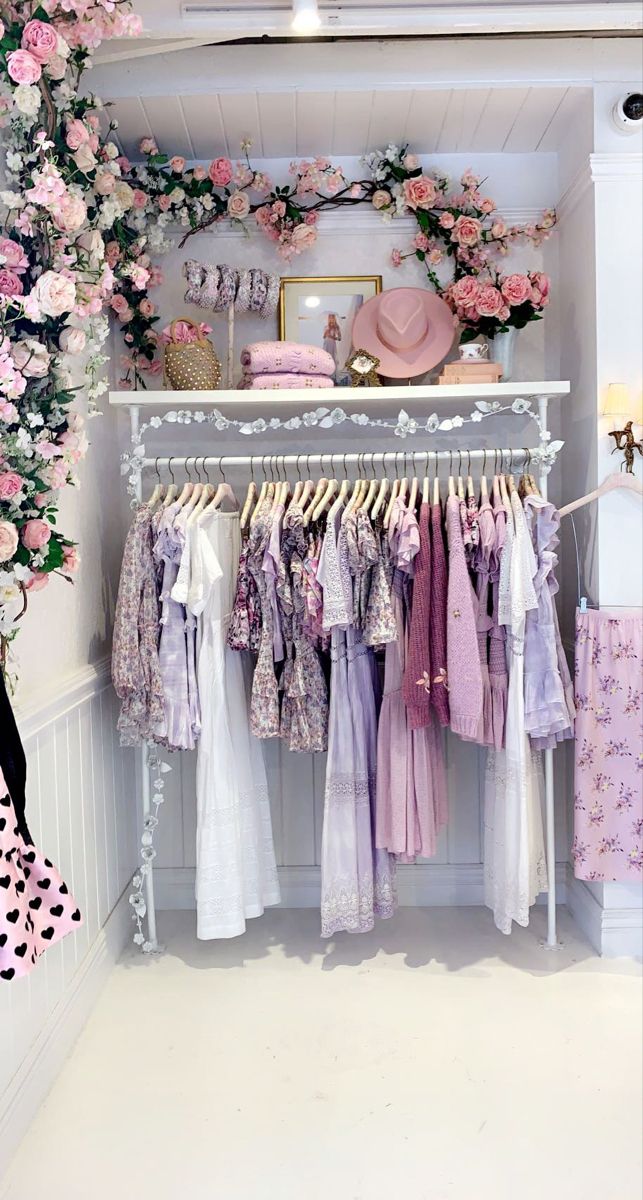 a clothing rack with clothes hanging on it and pink flowers in the corner behind it