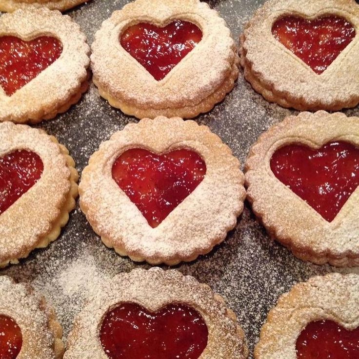 heart shaped cookies with powdered sugar and jelly in the middle on a baking sheet