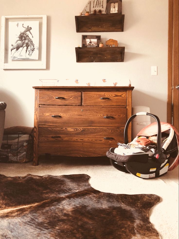 a baby in a car seat next to a dresser and shelf with pictures on it