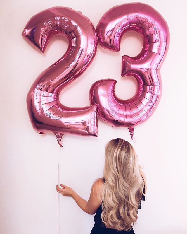 a woman standing in front of a large number twenty two balloon set on the wall