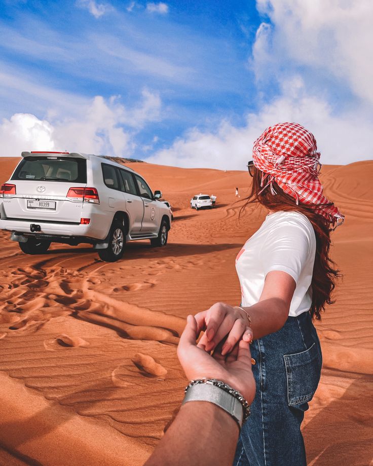 a man and woman holding hands in the desert with cars driving by on sand dunes