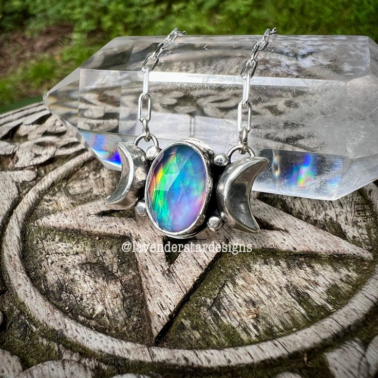 A faceted aurora opal (synthetic) and quartz doublet cradled in sterling and fine silver adorned in stars. Two solid silver crescent moons sit on either side of the stone. It's suspended from an 18-inch sterling silver chain with a lobster clasp. Pendant measures 26x16mm. Metaphysical Meaning of Quartz: Quartz is known as the “Master Healer” and is revered for its ability to amplify energy and thought. It harmonizes and aligns the chakras, promoting clarity and balance. This crystal is believed to enhance spiritual growth, increase wisdom, and foster a deep connection to the universe. Wearing this pendant may help you tap into the boundless energy of the cosmos, bringing a sense of peace, love, and enlightenment to your life. Items are handcrafted and you will likely see marks left by my t Mystical Oval Moon Phase Jewelry, Silver Moon-shaped Magical Necklace, Magical Moon-shaped Sterling Silver Necklace, Magical Moon Shaped Sterling Silver Necklace, Magical Silver Moon Jewelry, Iridescent Sterling Silver Spiritual Jewelry, Iridescent Oval Sterling Silver Jewelry, Mystical Nickel-free Moonstone Jewelry, Celestial Silver Moonstone Necklace