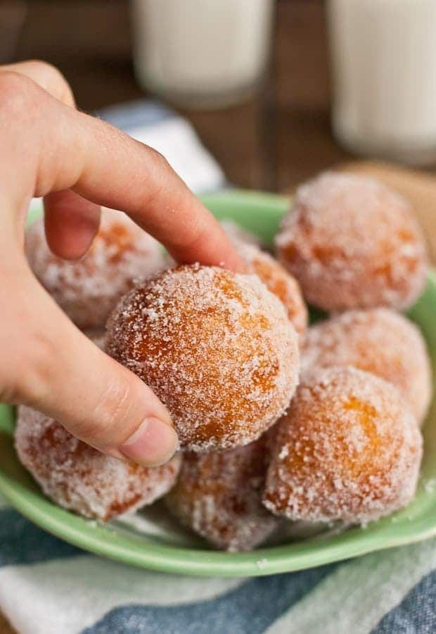 a person picking up sugar covered doughnuts from a green plate on a table