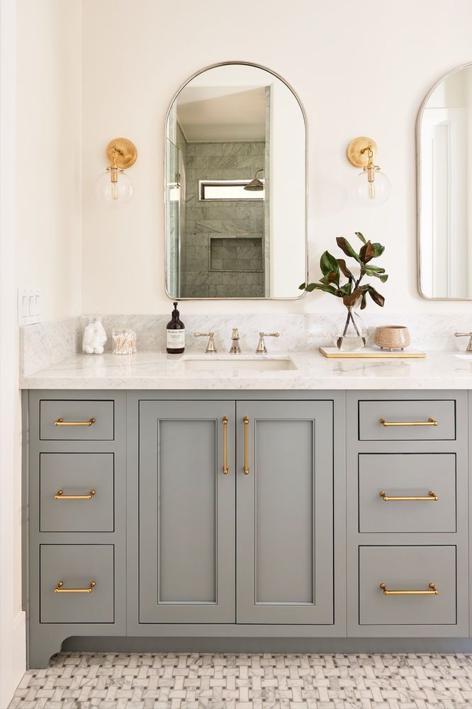 a bathroom vanity with two sinks, mirrors and lights on the wall above it is decorated in white and gold