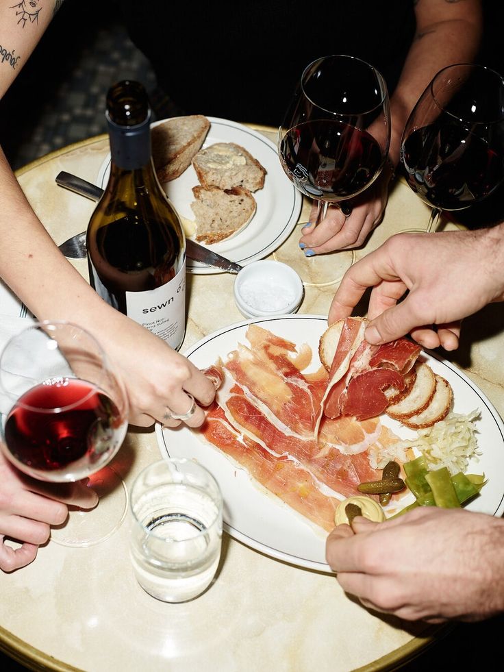 several people holding their hands over a plate with food and wine