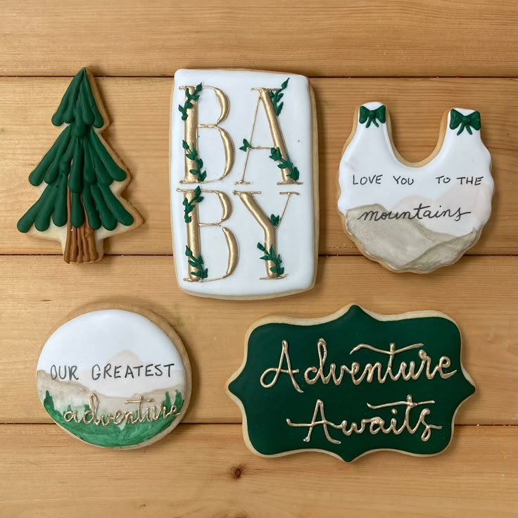 cookies decorated with green and white icing sitting on top of a wooden table next to baby's announcement magnets