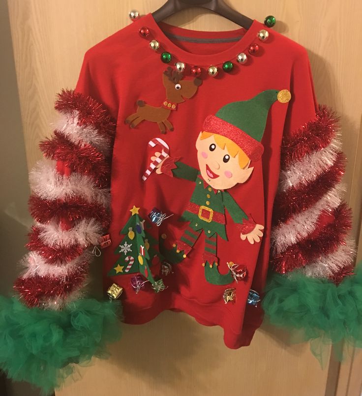 a christmas sweater hanging on a door with green and red tinsel trimmings