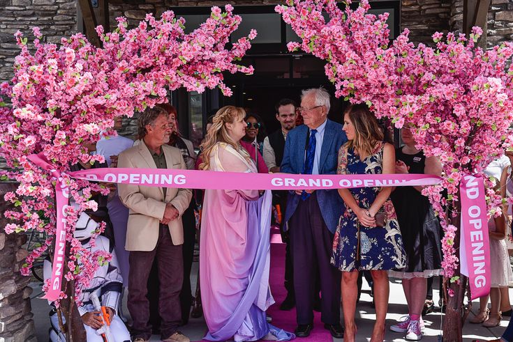 a group of people standing in front of a pink ribbon that says opening grand opening