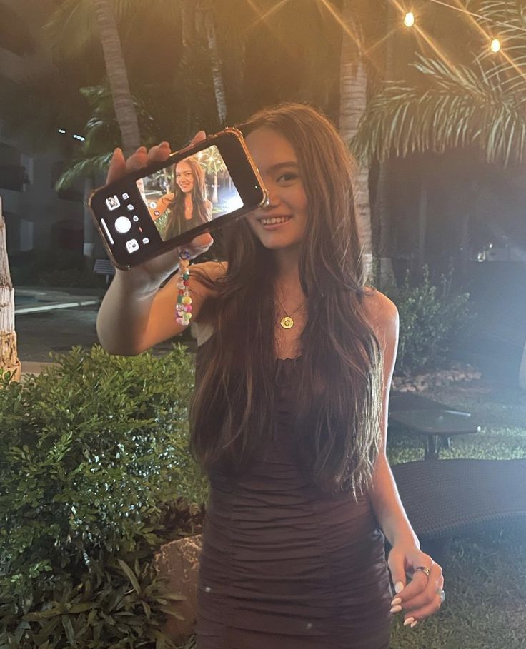 a woman taking a selfie with her cell phone while standing in front of a palm tree