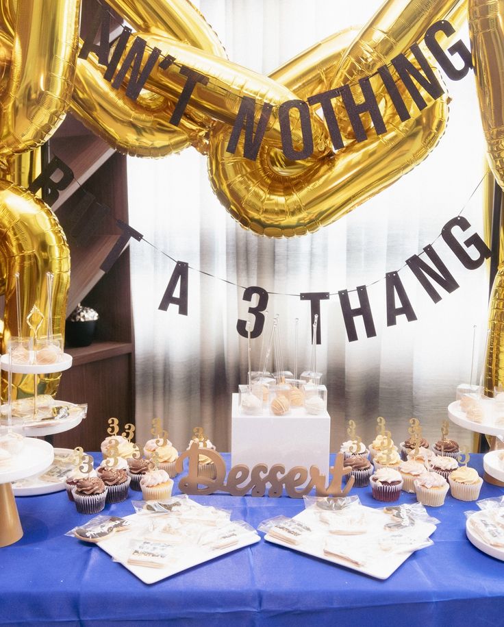 a table topped with lots of cupcakes and gold balloons