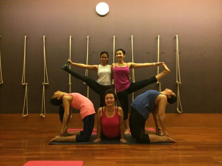 a group of women doing yoga poses in front of a wall with poles on it