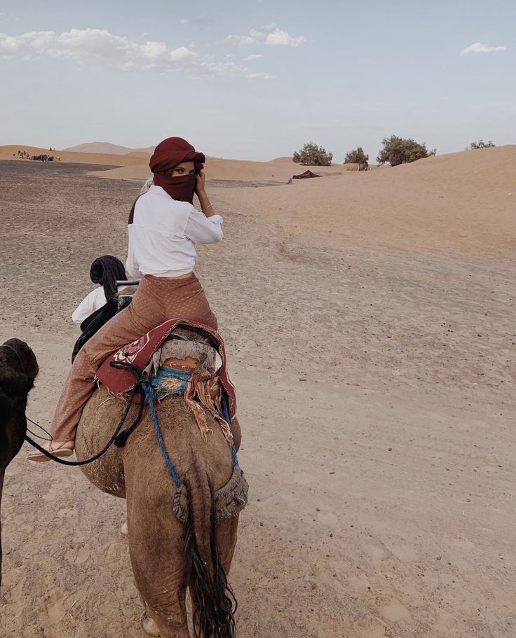 a woman riding on the back of a camel next to a dog in the desert