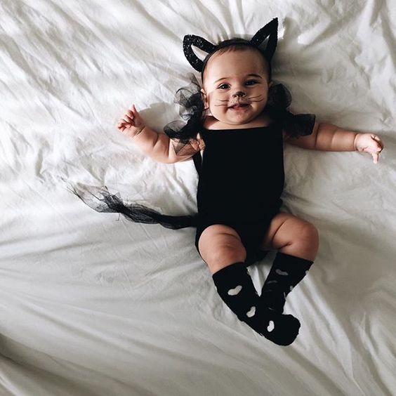 a baby dressed up as a cat laying on top of a white sheet covered bed