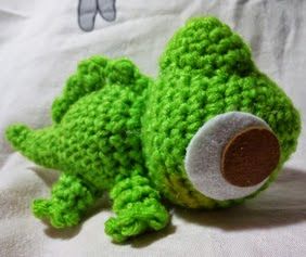 a green crocheted stuffed animal laying on top of a bed