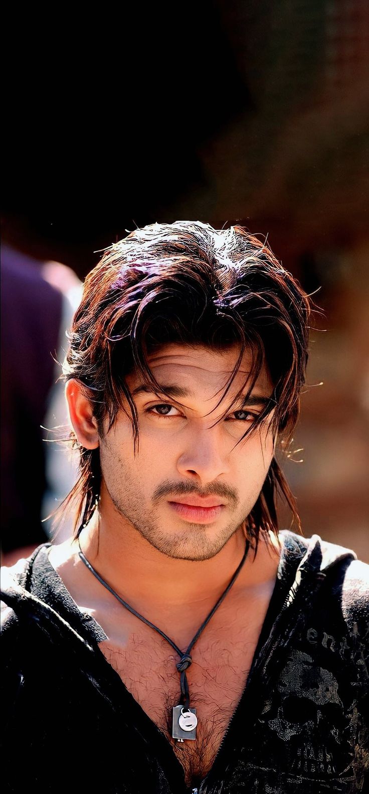 a close up of a person with long hair and a necklace on his neck looking at the camera