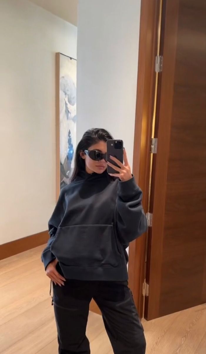 a woman taking a selfie in front of a mirror wearing sunglasses and black sweatpants