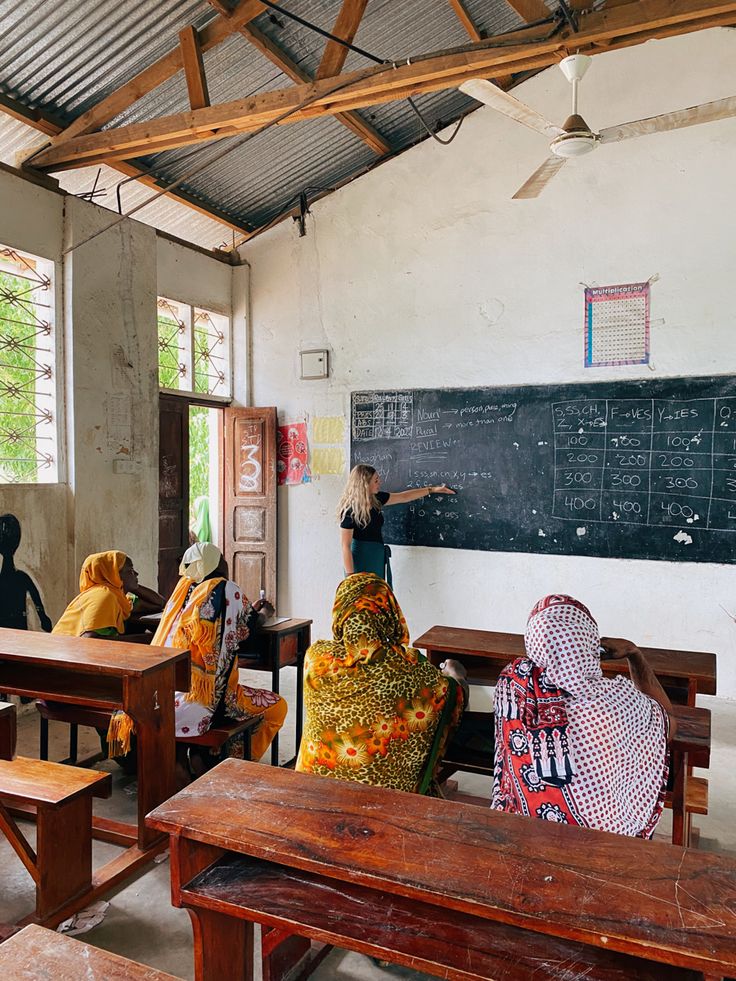 some people are sitting at desks and writing on a blackboard in a classroom