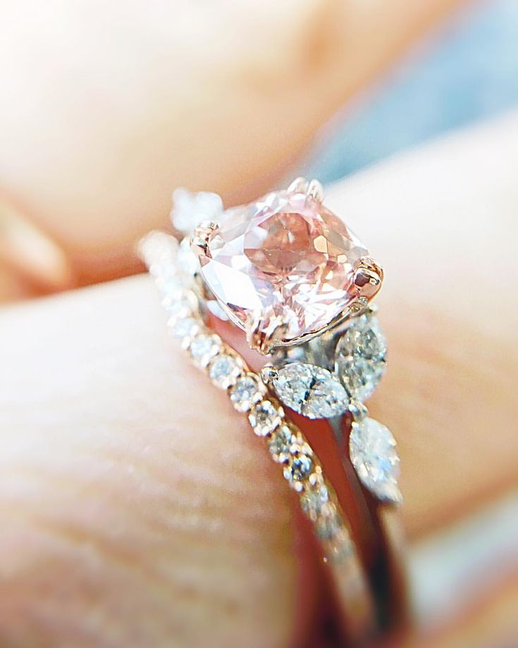 a woman's hand holding a ring with a pink diamond in the center and white diamonds around it