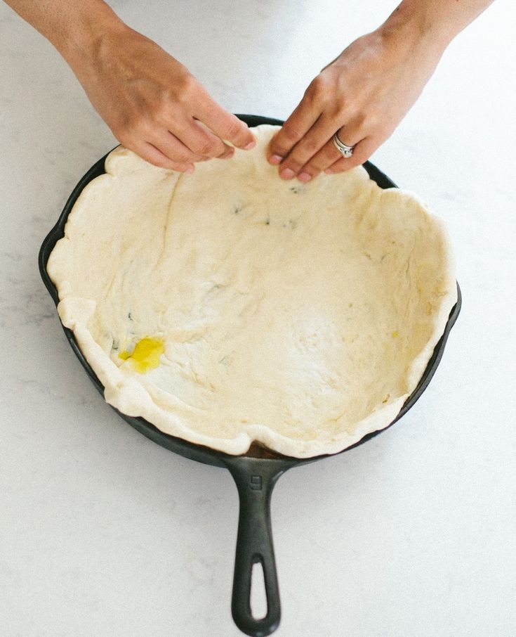 a person is making an uncooked pizza crust in a cast iron skillet