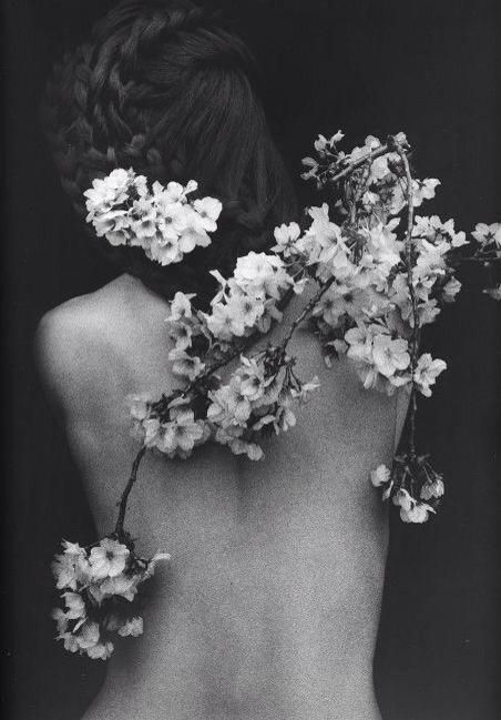 the back of a woman's body with flowers in her hair and behind her is a black and white photo