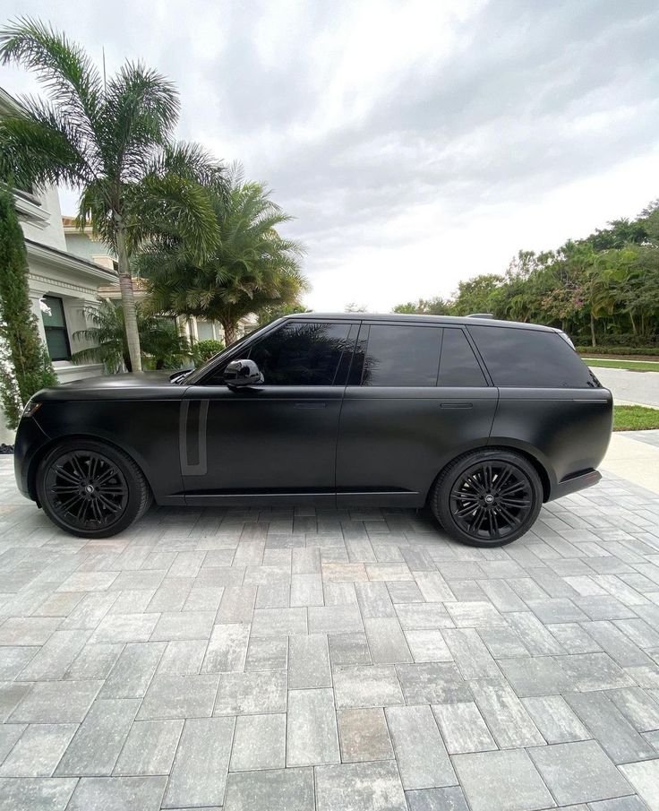 a black suv parked in front of a house on a brick driveway with palm trees