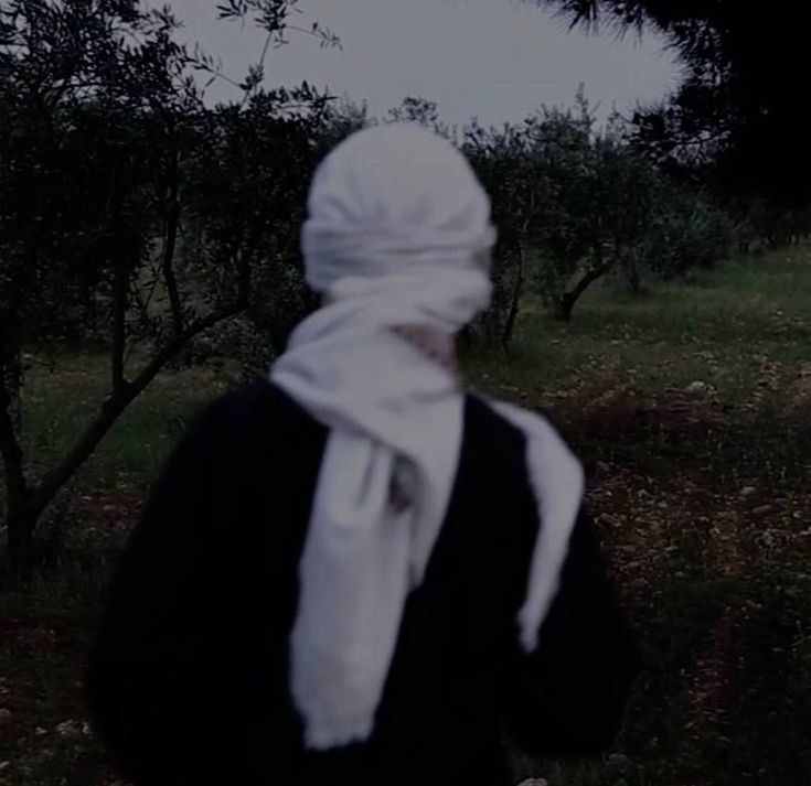 a person with a white scarf on their head is walking through an apple orchard in the dark