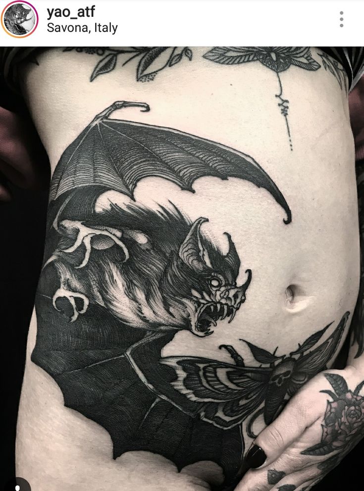 a woman's stomach with a bat tattoo on the side and her hand holding it