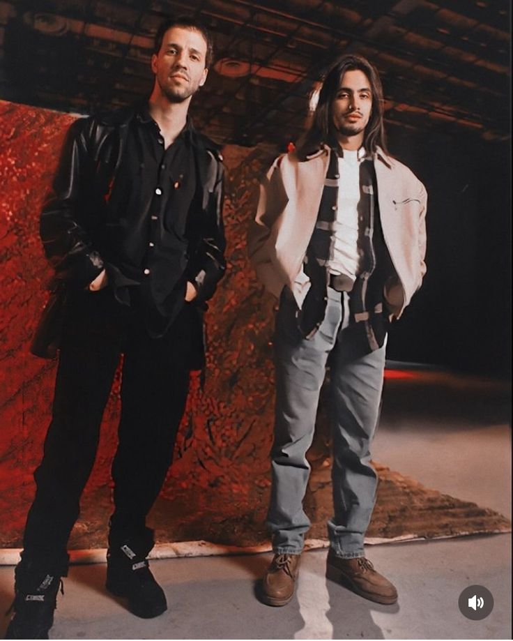 two men standing next to each other in front of a red wall