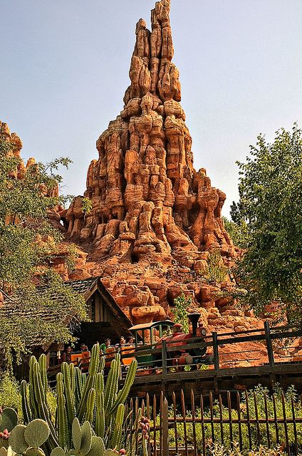 a very tall tower with many rocks on it's sides and cactus in the foreground