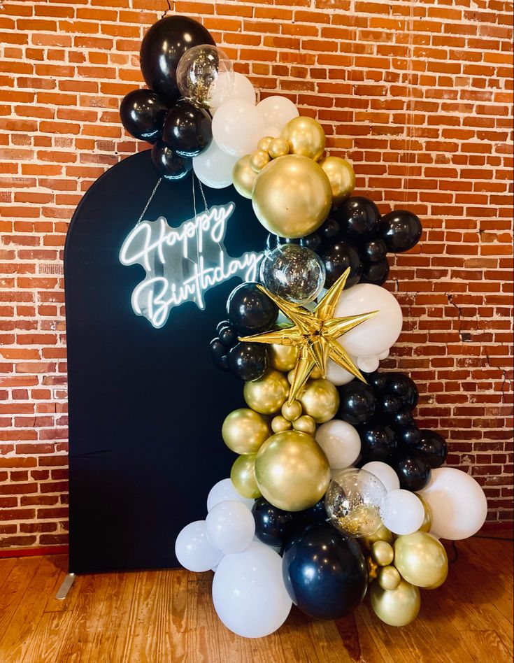 a happy birthday balloon arch with balloons and stars on the top in front of a brick wall