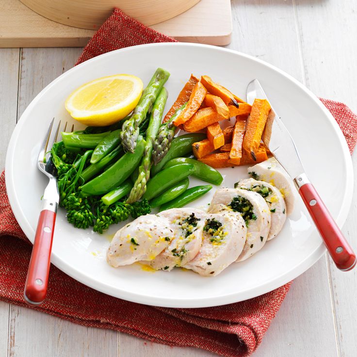 a white plate topped with chicken, broccoli and carrots next to lemon wedges