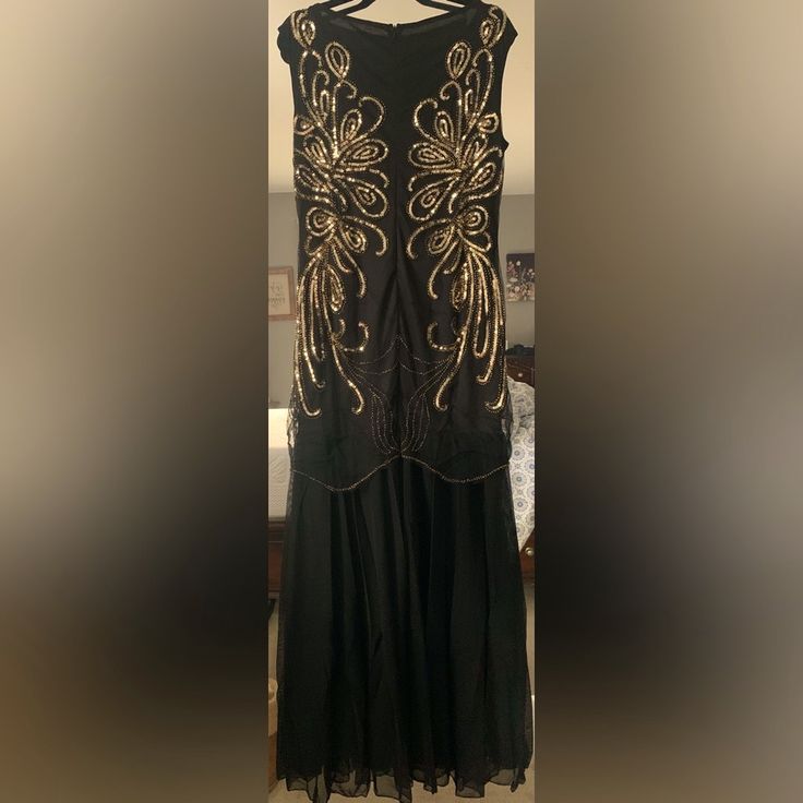 a black dress with gold embellishments is hanging on a hanger in a room