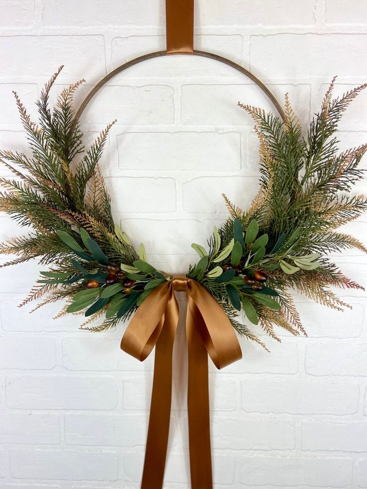 a wreath hanging on a brick wall with a brown ribbon around it and some greenery