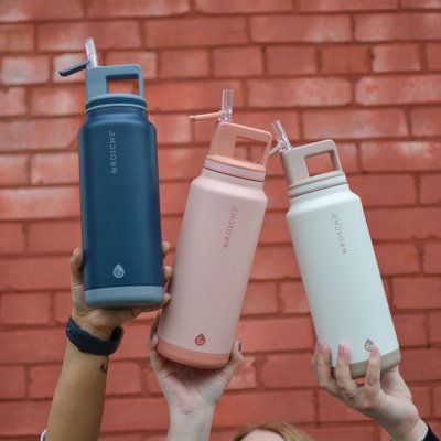 three people holding up two different colored water bottles in front of a red brick wall