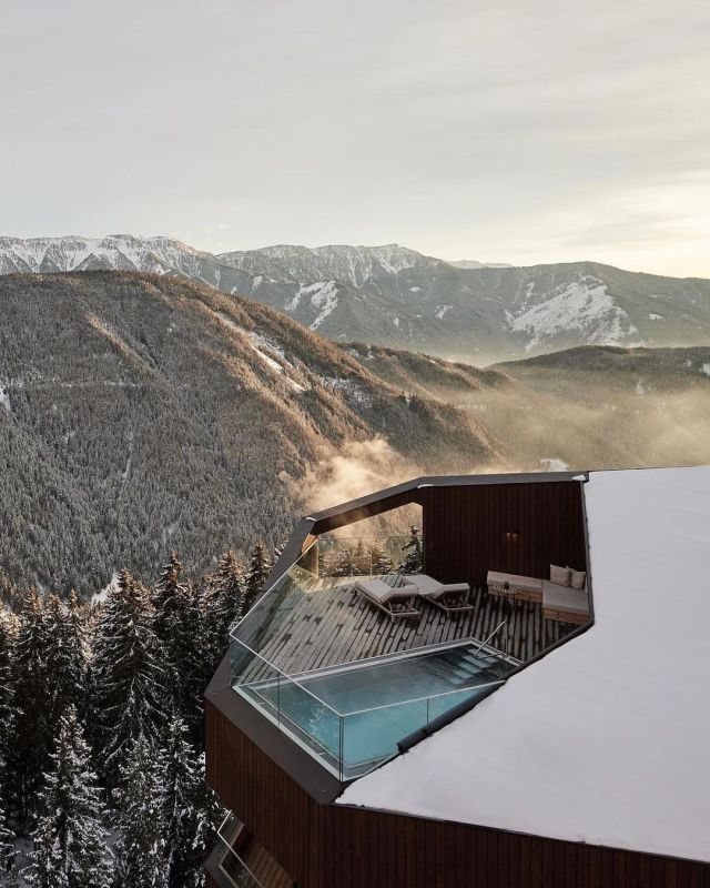 a hot tub on top of a snow covered roof next to trees and mountains in the background