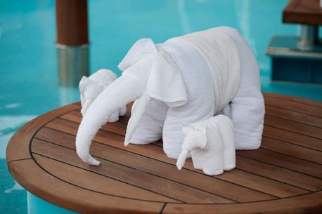 an elephant made out of towels sitting on top of a wooden table next to a swimming pool