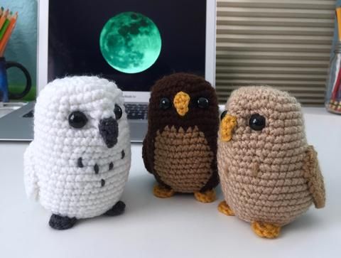 three crocheted owls sitting next to each other on a desk in front of a laptop