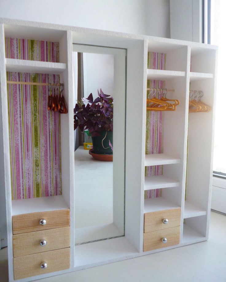 an open white bookcase with two drawers and a mirror on the wall next to a potted plant