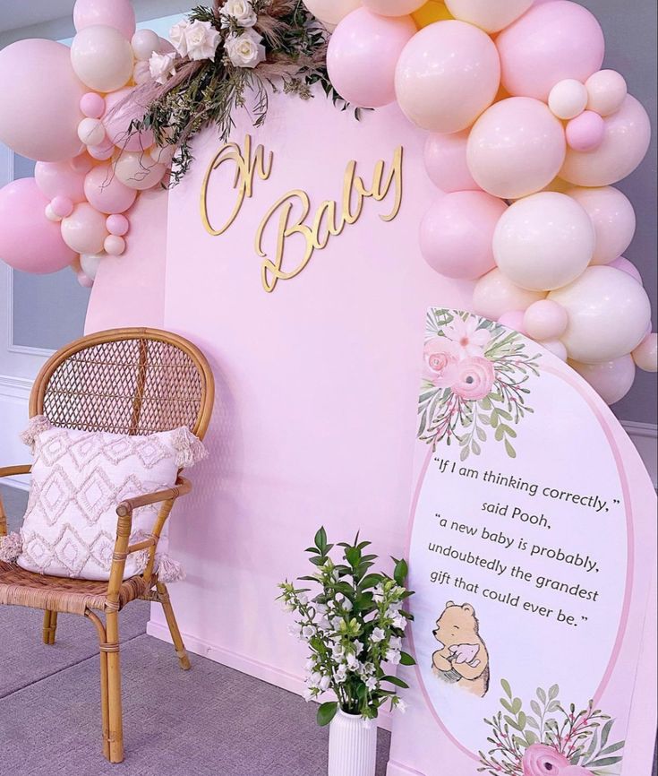 a baby shower with balloons and flowers on the wall next to a wicker chair