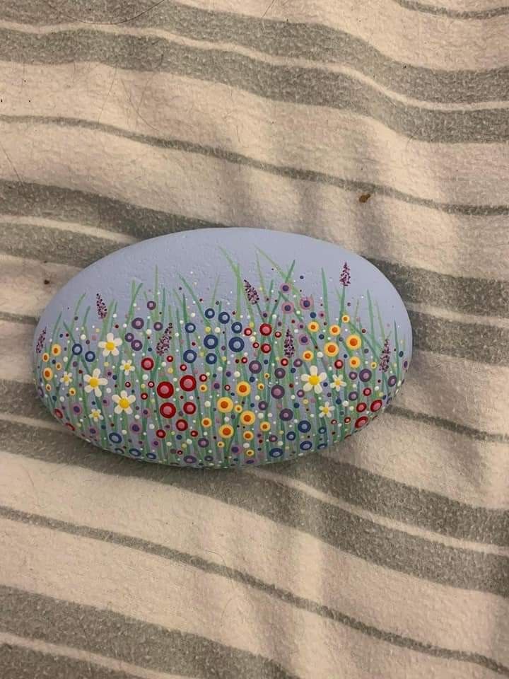 a painted rock sitting on top of a bed covered in grass and wildflowers