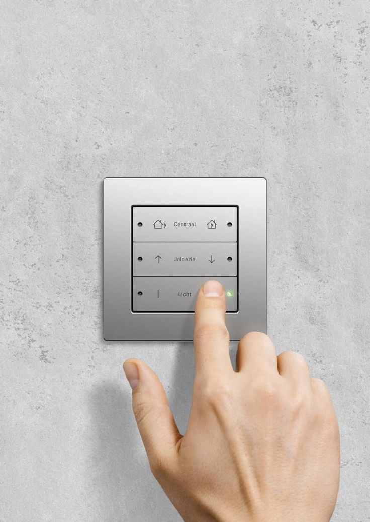 a person pressing the button on a wall mounted light switch with one hand and pointing at it