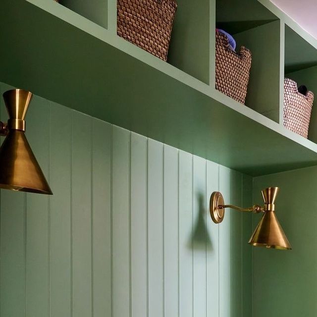 two brass lamps are on the wall in a green room with white walls and shelves