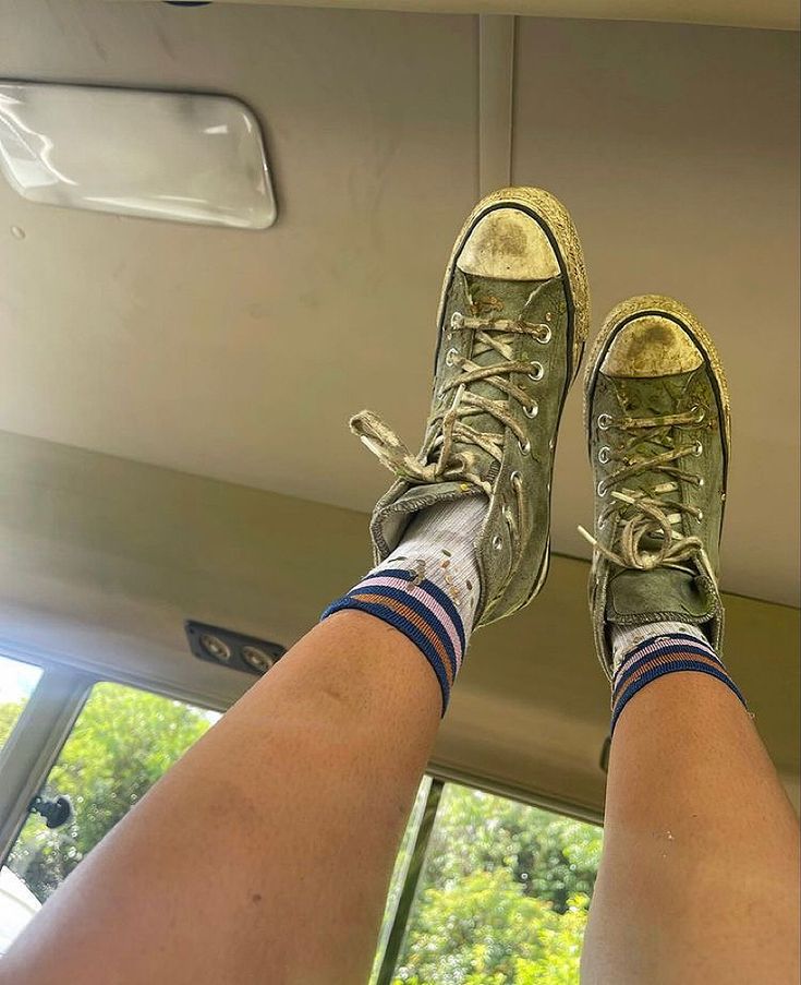 the legs and feet of a person wearing green tennis shoes on a bus with trees in the background