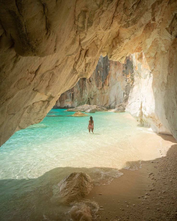 a person standing in the water near a cave