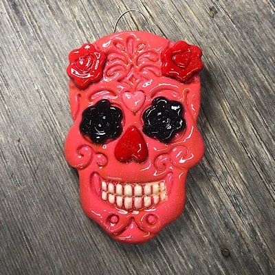 a red sugar skull ornament with black eyes and roses on its head, sitting on a wooden surface