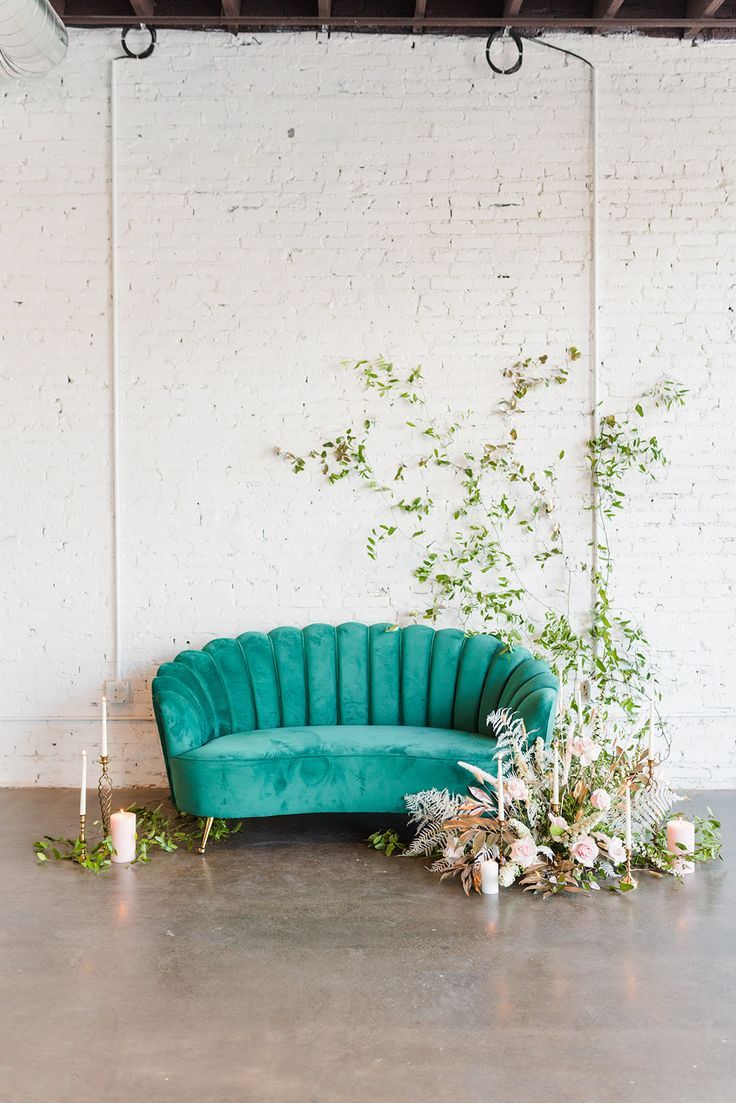 a green couch sitting on top of a wooden floor next to a white brick wall